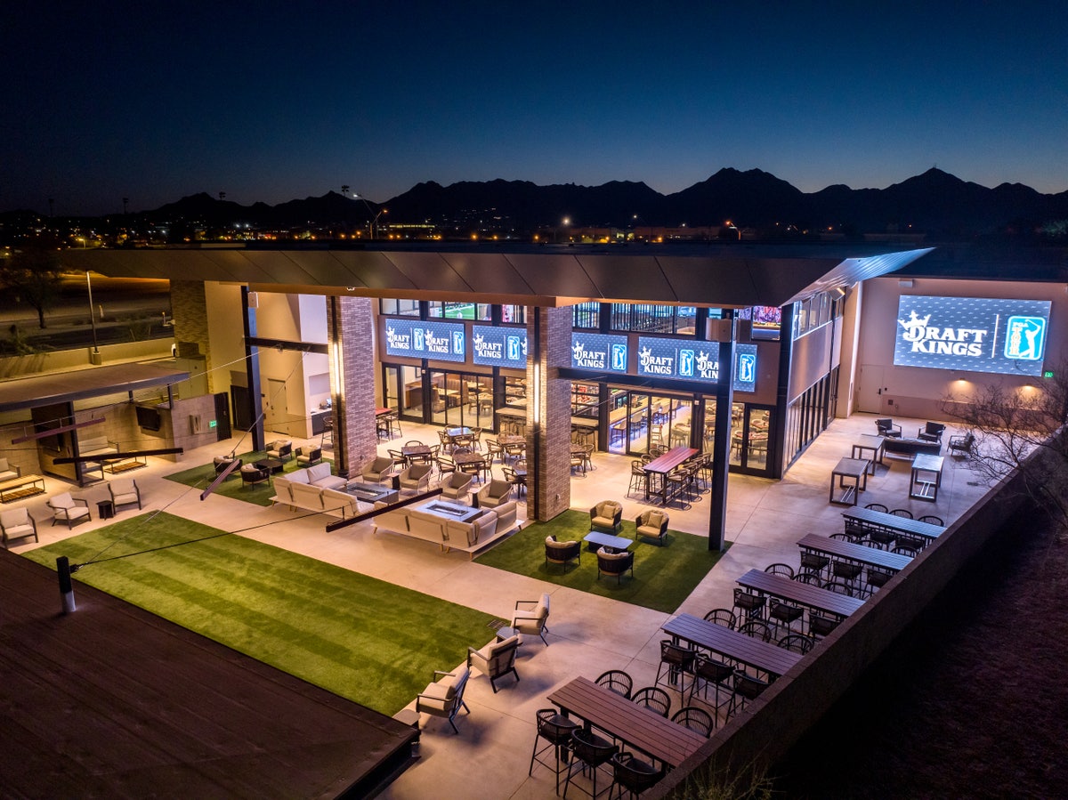 Modern entertainment venue with outdoor seating, turf lawn, and mountain views at dusk